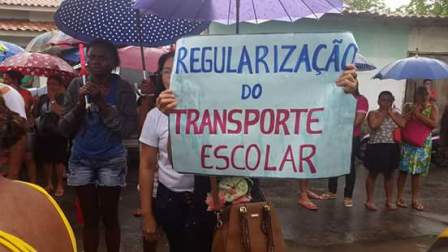 Funcionária exibe cartaz cobrando regularização do transporte escolar